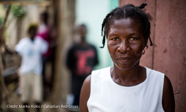 Une femme haïtienne vêtue d’un débardeur blanc regarde droit vers la caméra